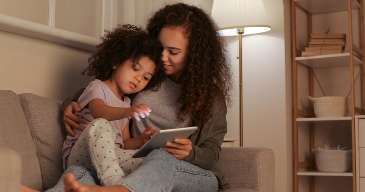 Parent and child using a small tablet on a couch, representing reading and family tablet use