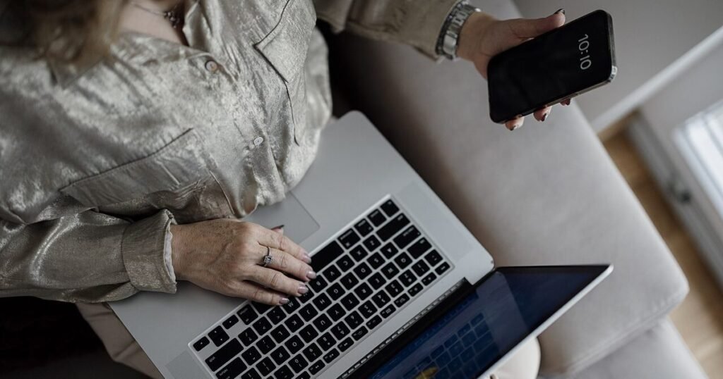 Person using a laptop and smartphone while checking phone backup settings